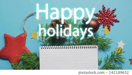 Displaying spiral notebook centered on blue surface with pine sprigs, pinecone, Happy holidays text Displaying spiral notebook centered on blue surface with pine sprigs, pinecone, Happy holidays text 142189632
