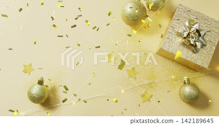 Featuring gold gift box with metallic bow sitting on right cream tabletop, with baubles, copy space Featuring gold gift box with metallic bow sitting on right cream tabletop, with baubles, copy space 142189645