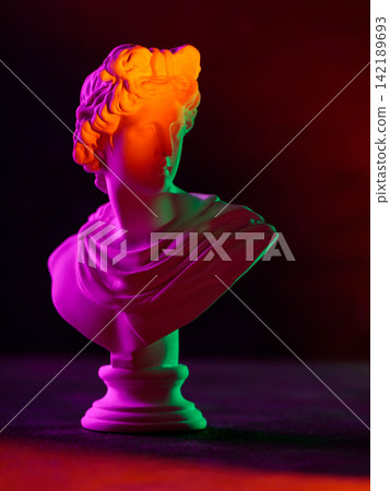 Classical sculpture bust illuminated with vibrant neon lighting on dark background Classical sculpture bust illuminated with vibrant neon lighting on dark background 142189693