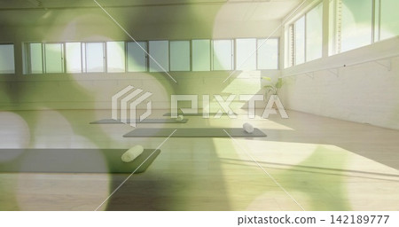 Displaying empty yoga studio featuring dark mats on wood floor, featuring windows and rolled towels 142189777