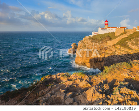 Cabo de Sao Vicente lighthouse at sunrise beyond golden foreground rocks Cabo de Sao Vicente lighthouse at sunrise beyond golden foreground rocks 142190839