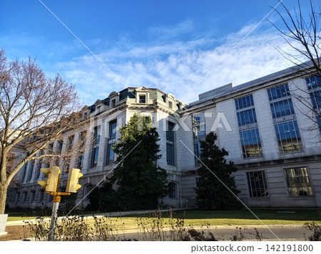 The historic Russell State Senate Office Building, constructed of white stone, features a Beaux-Arts facade with dormers and evergreen trees. 142191800