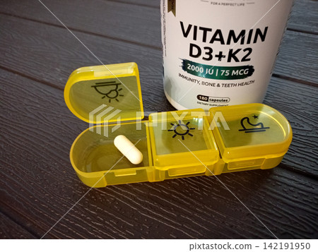 On the table is a medication organizer with vitamin D capsule in front and a jar On the table is a medication organizer with vitamin D capsule in front and a jar 142191950