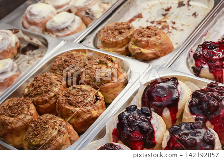Cinnabons in showcase. Cinamon buns in  Cinnamon rolls with nuts and fruits, isolated. Sweet dessert variaty. Fresh bakery in cafe. Decorated muffins in restaurant. Sweet breakfast conept.  142192057