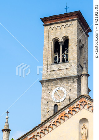 Ancient Church of Saint Thecla in Torno Facade with Clock Tower near Lake Shore behind a Ferry Pier Como Italy Ancient Church of Saint Thecla in Torno Facade with Clock Tower near Lake Shore behind a Ferry Pier Como Italy 142192303