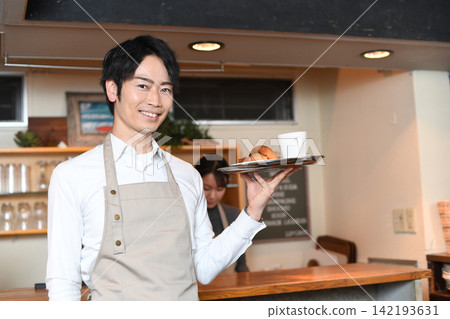 一位微笑的男服務生正在咖啡館為顧客上菜。 一位微笑的男服務生正在咖啡館為顧客上菜。 142193631