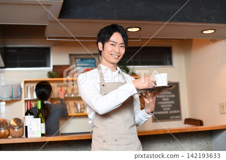 一位微笑的男服務生正在咖啡館為顧客上菜。 一位微笑的男服務生正在咖啡館為顧客上菜。 142193633