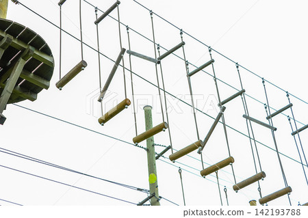 High suspension bridge in a rope amusement park, obstacle course for children in a rope park High suspension bridge in a rope amusement park, obstacle course for children in a rope park 142193788
