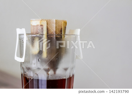 Coffee in a drip filter bag brews in a cup on the kitchen counter 142193790