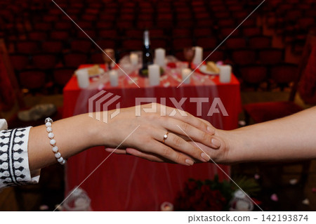 Close up of couple holding hands with engagement ring at romantic candlelit dinner with red table cloth. Close up of couple holding hands with engagement ring at romantic candlelit dinner with red table cloth. 142193874
