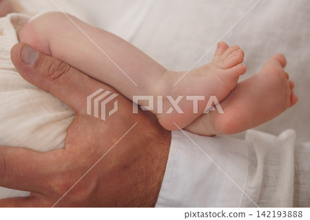 Close up of a man holding a newborn baby leg and foot in soft white light. Close up of a man holding a newborn baby leg and foot in soft white light. 142193888