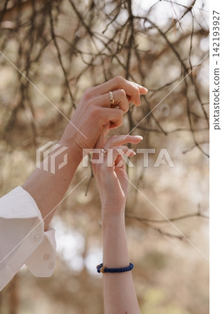 Couple holding hands with gold rings against a blurred natural background of winter tree branches. 142193927