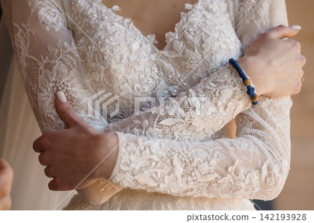 Close up of bride wearing long sleeve lace wedding dress and blue beaded bracelet with arms crossed Close up of bride wearing long sleeve lace wedding dress and blue beaded bracelet with arms crossed 142193928