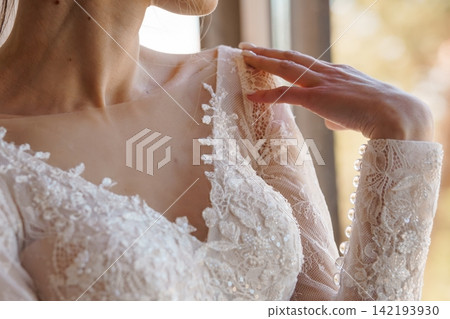 Close up of a woman wearing a white lace bridal gown with intricate embroidery and sequin details. Close up of a woman wearing a white lace bridal gown with intricate embroidery and sequin details. 142193930