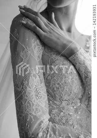 Close up of woman in intricate floral lace wedding dress with hand on shoulder in monochrome style Close up of woman in intricate floral lace wedding dress with hand on shoulder in monochrome style 142193931