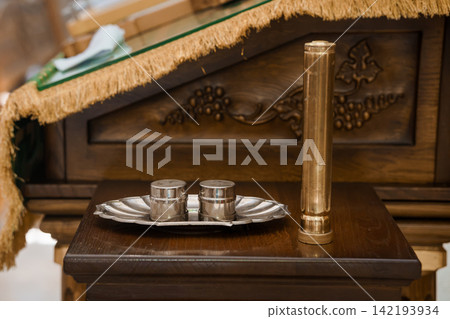 Silver communion cups and gold liturgical candle on a carved wooden altar in a church interior. Silver communion cups and gold liturgical candle on a carved wooden altar in a church interior. 142193934