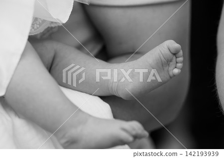 Close up of newborn baby feet resting on adult leg in black and white artistic style. 142193939
