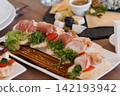 Gourmet appetizers with cured meats and fresh greens on a white platter with balsamic glaze and sesame seeds. 142193942