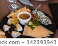 Gourmet cheese platter with brie, blue cheese, sliced cheddar, honey, grapes and walnuts on black slate board. 142193943
