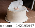 White frosted baby shower cake topped with a sleeping infant figure and large angel wings on a brown table. 142193947
