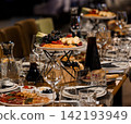 Fresh Fruit Platter and Gourmet Appetizers on a Dining Table with Red Wine in Glass Decanters 142193949