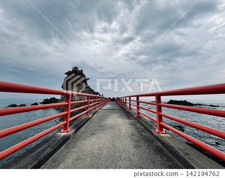 A seaside bridge with red railings and a cloudy sky. 142194762