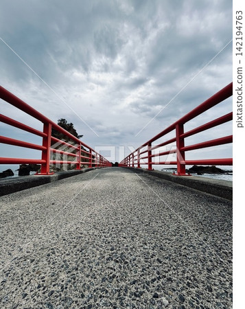A symmetrical landscape captured from a low angle, showing a bridge with red railings. A symmetrical landscape captured from a low angle, showing a bridge with red railings. 142194763