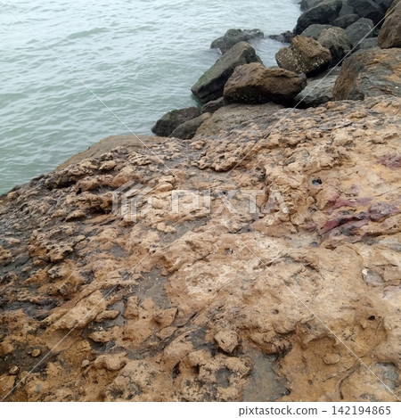 Scenic View Of A Rocky Ocean Shoreline Showing Large Weathered Boulders Acting As A Natural Breakwater Against Gentle Sea Scenic View Of A Rocky Ocean Shoreline Showing Large Weathered Boulders Acting As A Natural Breakwater Against Gentle Sea 142194865