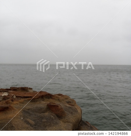 Artistic Out Of Focus Rough Rock Foreground Contrasting With A Sharp Distant Horizon Over A Calm Moody Overcast Ocean Sea Artistic Out Of Focus Rough Rock Foreground Contrasting With A Sharp Distant Horizon Over A Calm Moody Overcast Ocean Sea 142194866