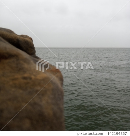 Abstract Coastal Composition Featuring A Blurred Rock Edge On The Left Beside A Vast Calm Ocean Under A Moody Overcast Sky Abstract Coastal Composition Featuring A Blurred Rock Edge On The Left Beside A Vast Calm Ocean Under A Moody Overcast Sky 142194867