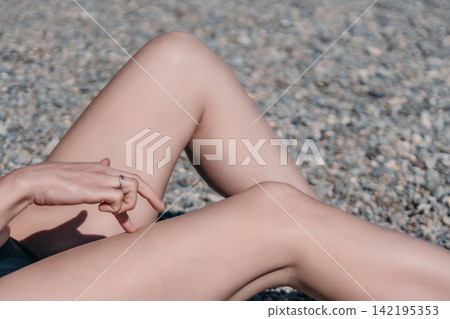 Woman, legs, hand, close-up shot of a woman relaxing on a pebbled beach during a sunny summer day, lifestyle concept Woman, legs, hand, close-up shot of a woman relaxing on a pebbled beach during a sunny summer day, lifestyle concept 142195353