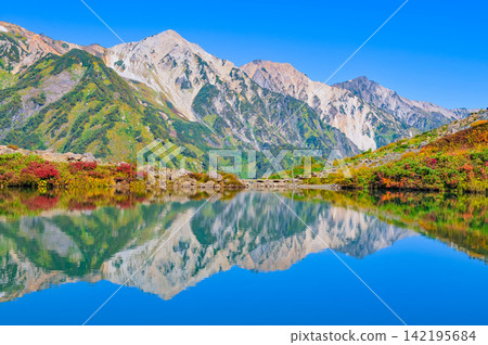 在一個晴朗的秋日早晨，白馬山脈完美地對稱地倒映在八方池廣闊如鏡的水面上，形成了一幅無人居住的景象。 142195684