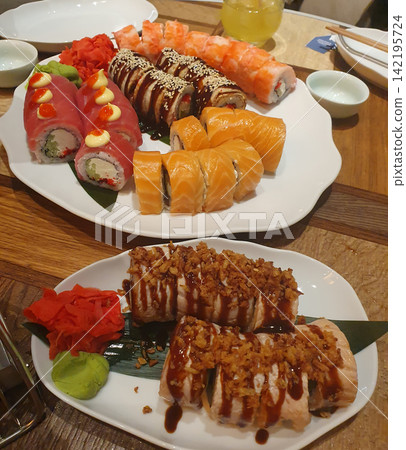 Large set of assorted sushi and rolls with salmon, tuna, eel, wasabi and ginger on white plates. Asian cuisine, sushi bar 142195724