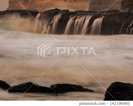 Long exposure photography of silky smooth water cascading over rocky cliff terraces at Klayar Beach (Pantai Klayar) during warm golden hour sunset, Pacitan, East Java, Indonesia. Long exposure photography of silky smooth water cascading over rocky cliff terraces at Klayar Beach (Pantai Klayar) during warm golden hour sunset, Pacitan, East Java, Indonesia. 142196993