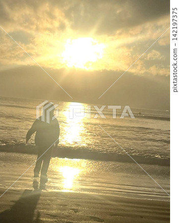 The silhouette of a child walking along the beach, illuminated by the setting sun. The silhouette of a child walking along the beach, illuminated by the setting sun. 142197375