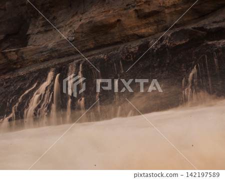 Close-up long exposure shot of silky smooth water cascading over dark rocky ledges at Klayar Beach (Pantai Klayar), Pacitan, East Java, Indonesia. Close-up long exposure shot of silky smooth water cascading over dark rocky ledges at Klayar Beach (Pantai Klayar), Pacitan, East Java, Indonesia. 142197589