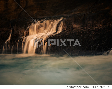 Close-up long exposure shot of silky smooth water cascading over dark rocky ledges at Klayar Beach (Pantai Klayar), Pacitan, East Java, Indonesia. Close-up long exposure shot of silky smooth water cascading over dark rocky ledges at Klayar Beach (Pantai Klayar), Pacitan, East Java, Indonesia. 142197594