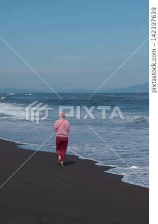 Woman walks along black volcanic shoreline facing Pacific Ocean waves in Kamchatka. Travel, coastal lifestyle, nature tourism, solitude, exploration, outdoor recreation, summer vacation. Woman walks along black volcanic shoreline facing Pacific Ocean waves in Kamchatka. Travel, coastal lifestyle, nature tourism, solitude, exploration, outdoor recreation, summer vacation. 142197639