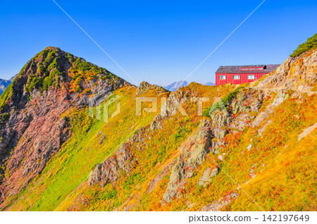 A mountain landscape viewed from the hiking trail of Mt. Karamatsu, looking back at the building of the Karamatsu Summit Mountain Hut on a clear autumn morning. A mountain landscape viewed from the hiking trail of Mt. Karamatsu, looking back at the building of the Karamatsu Summit Mountain Hut on a clear autumn morning. 142197649