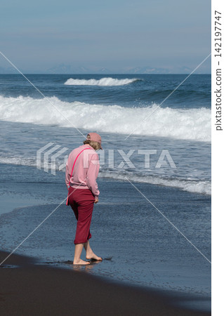 Barefoot woman walks by Pacific waves on black sand at Khalaktyrsky Beach, Kamchatka, Russia. Travel, coastal lifestyle, nature tourism, solitude, summer vacation, outdoor recreation. Barefoot woman walks by Pacific waves on black sand at Khalaktyrsky Beach, Kamchatka, Russia. Travel, coastal lifestyle, nature tourism, solitude, summer vacation, outdoor recreation. 142197747