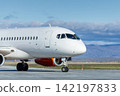 Close up to the front of the white passenger plane taxiing at the airport against a mountain range 142197833