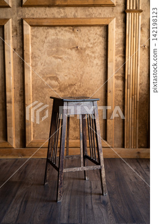 Vintage wooden stool standing on dark parquet floor against brown paneled wall in interior setting  142198123