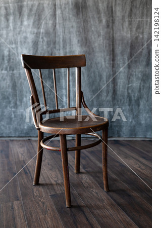 Vintage wooden chair on dark hardwood floor against textured grey canvas backdrop in minimalist photo studio space. 142198124