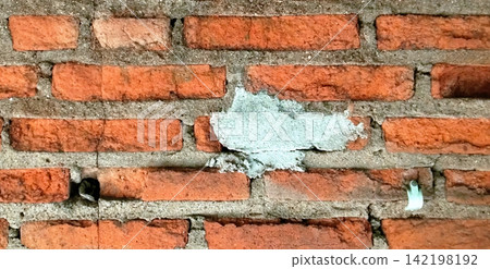 Damaged red brick wall with cement patches. 142198192