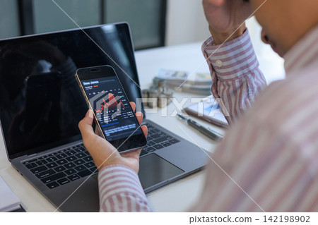 Worried businessman tracking a severe market downturn on a smartphone at his office desk. Worried businessman tracking a severe market downturn on a smartphone at his office desk. 142198902