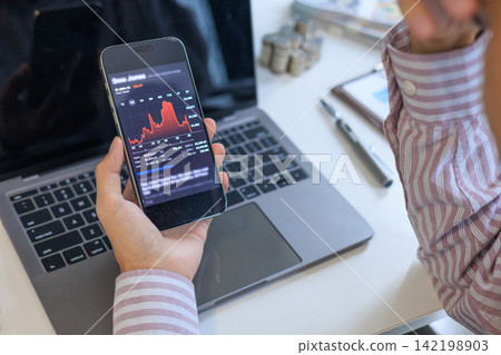 Worried businessman tracking a severe market downturn on a smartphone at his office desk. Worried businessman tracking a severe market downturn on a smartphone at his office desk. 142198903