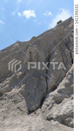 limestone cliffs and eroded rock formations under a cloudy blue sky, creating a dramatic natural landscape and geological vertical background. limestone cliffs and eroded rock formations under a cloudy blue sky, creating a dramatic natural landscape and geological vertical background. 142199281