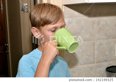 The boy is drinking from a cup. The boy is drinking from a cup. 142199325