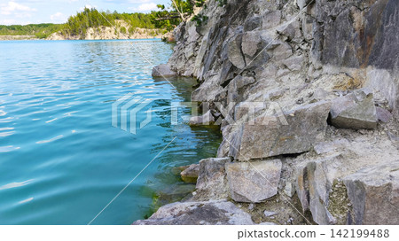 A turquoise quarry lake with rocky cliffs and lush green forest in summer, clear water, a rugged shoreline and a tranquil natural landscape, perfect for exploring and relaxing in nature. A turquoise quarry lake with rocky cliffs and lush green forest in summer, clear water, a rugged shoreline and a tranquil natural landscape, perfect for exploring and relaxing in nature. 142199488