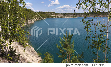 Scenic blue quarry lake surrounded by birch and pine trees, rocky cliffs and lush forest under a bright summer sky, creating a peaceful natural landscape for travel and outdoor concepts. Scenic blue quarry lake surrounded by birch and pine trees, rocky cliffs and lush forest under a bright summer sky, creating a peaceful natural landscape for travel and outdoor concepts. 142199490